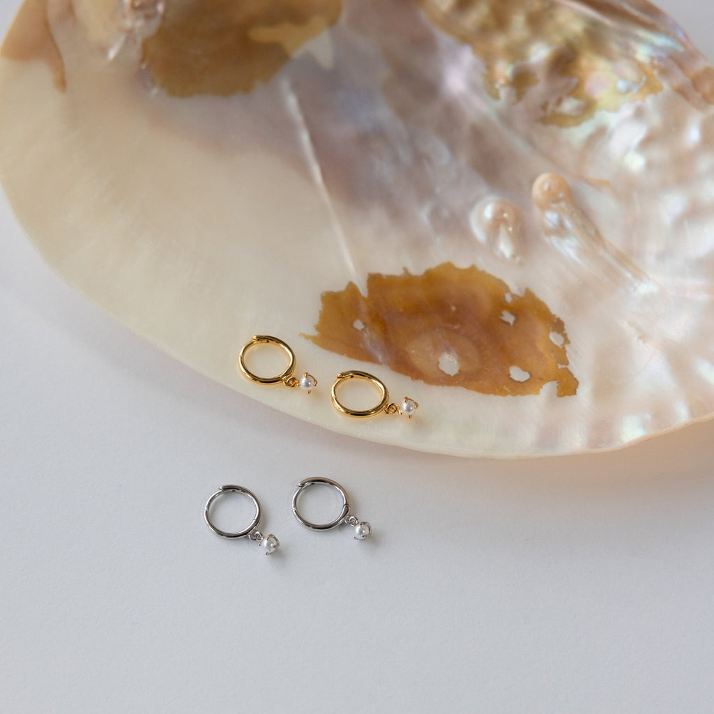 The Molly Pearl Huggies in Sterling Silver are elegantly displayed resting on a shell.