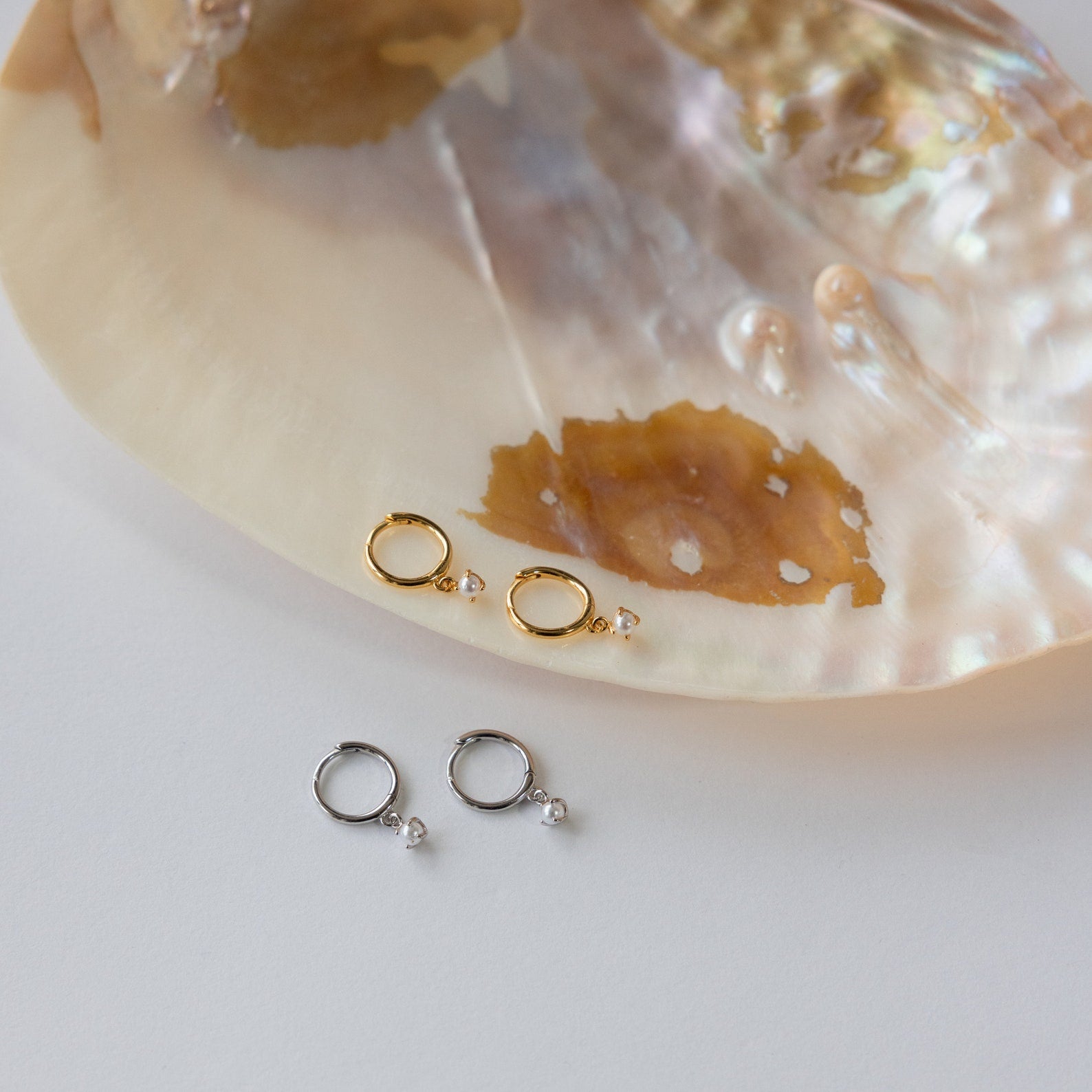 The Molly Pearl Huggies in Sterling Silver are elegantly displayed resting on a shell.