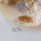 Two pairs of Molly Pearl Huggies, one gold and one silver, displayed on a large iridescent seashell.