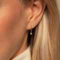 A close-up of a woman's ear adorned with the elegant Molly Pearl Huggies.