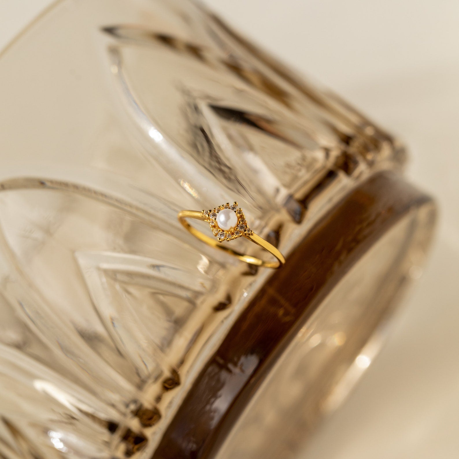 The Vintage Pave Pearl Ring shines elegantly on an ornate glass surface, highlighting the timeless charm and sophistication of this vintage-inspired piece.