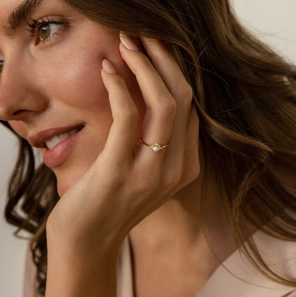 A woman with wavy brown hair displays the Vintage Pave Pearl Ring in Sterling Silver, hand softly touching her face—an elegant and timeless choice for a Christmas gift.