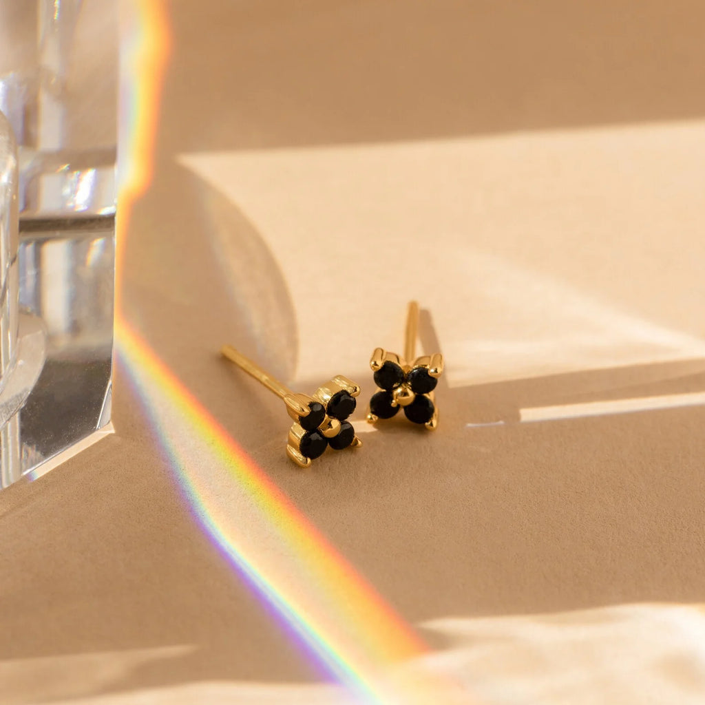 Onyx Diamond Earrings Set featuring small black stones on a beige surface, beside a prism casting a rainbow—ideal for those who appreciate the delicate charm of these elegant earrings.