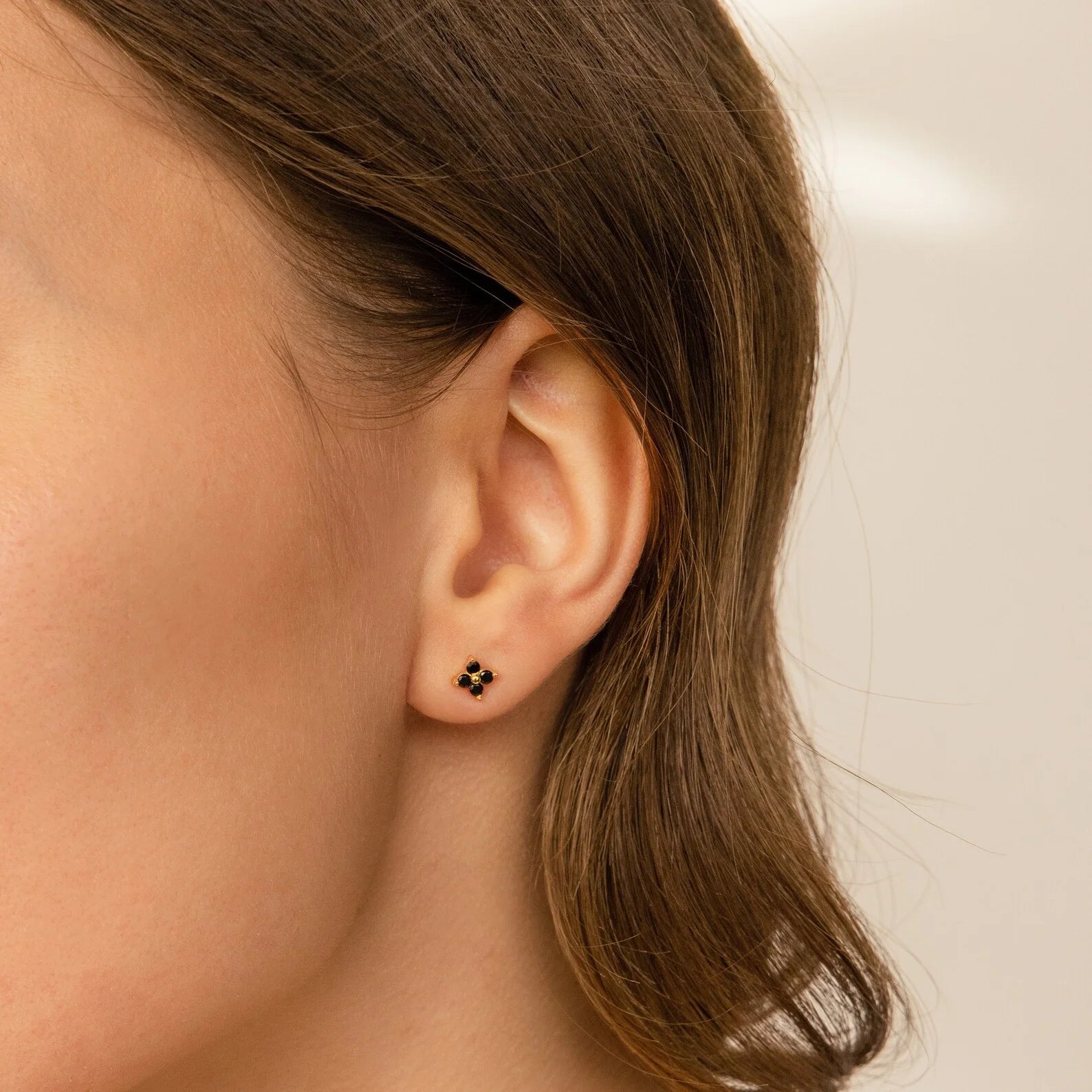 Close-up of a woman's ear wearing the Onyx Diamond Earrings Set—elegant gold and black studs—highlighted against a neutral background.