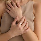 A woman in a sleeveless beige top crosses her arms, showcasing the Carrie Signet Ring—a custom engraved, minimalist accessory that adds a personal touch to her style.