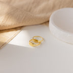 The Old English Signet Ring, a gold custom engraved piece with “11:11,” rests beside another gold band on a white surface and soft beige fabric—ideal for fans of personalized jewelry.