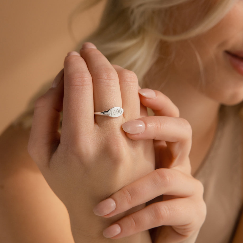 A woman smiles softly, displaying the Old English Signet Ring—a minimalist silver ring custom engraved with "1995" on its surface.
