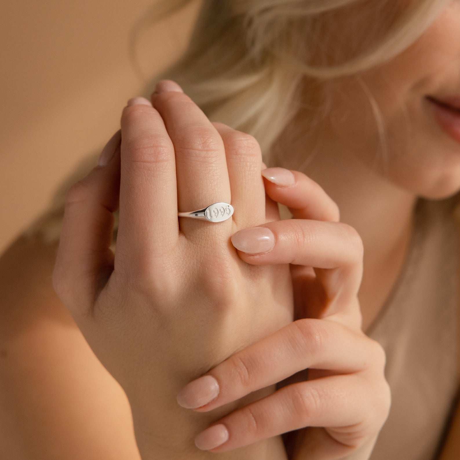 A woman smiles softly, displaying the Old English Signet Ring—a minimalist silver ring custom engraved with "1995" on its surface.