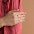 A hand wearing the Nella Duo Initial Ring rests on a pink-sleeved arm against a beige background—an elegant, personalized gift perfect for anniversaries.