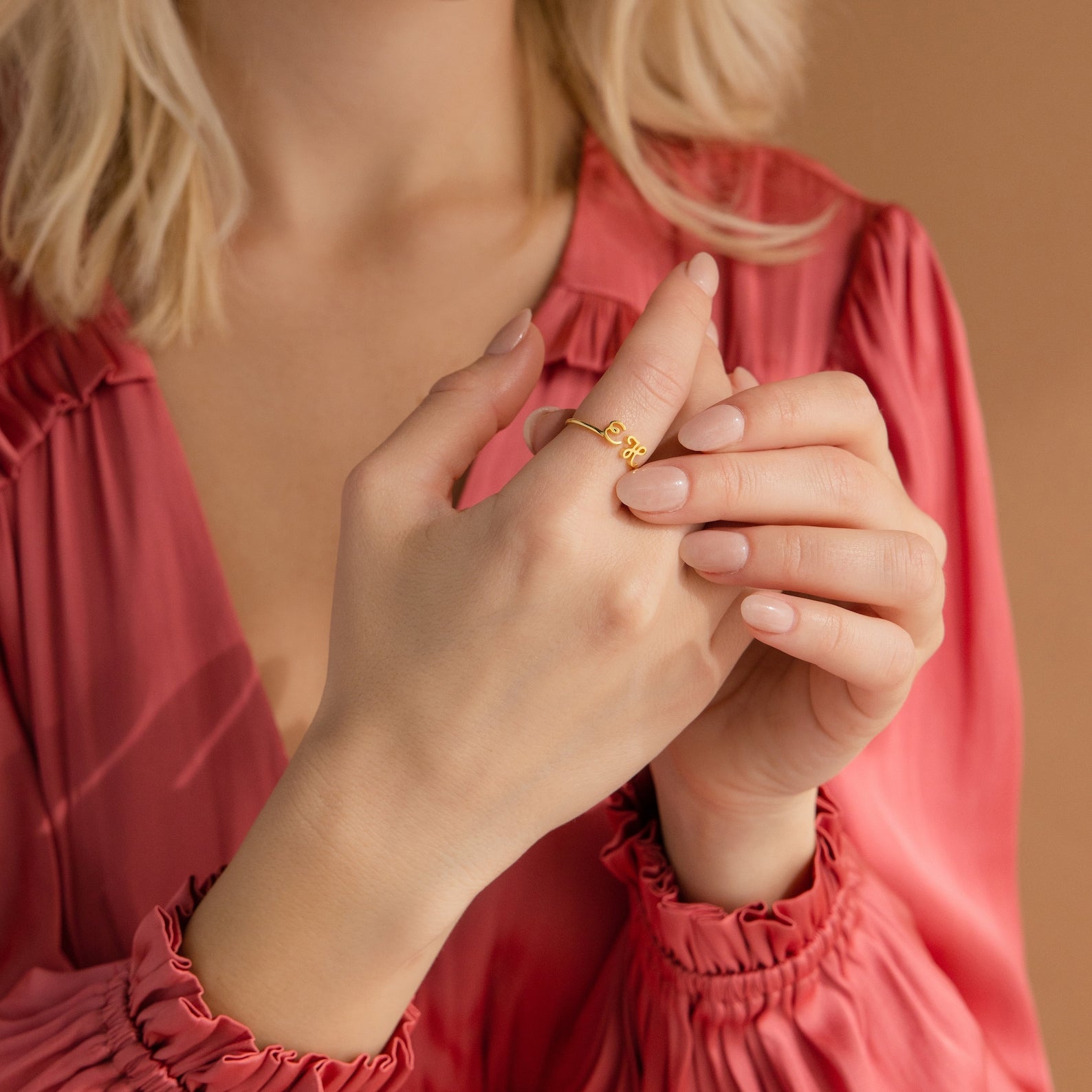 A woman in a pink blouse showcases the Dainty Duo Initial Ring on her finger, highlighting it as the perfect anniversary gift against a neutral backdrop.
