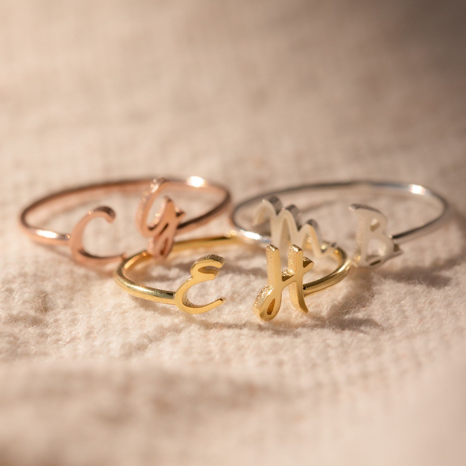 The Nella Duo Initial Ring—engraved with custom initials—rests on textured beige fabric, showcasing a personalized jewelry piece and a thoughtful anniversary gift.