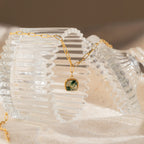 An Agate Pendant Necklace featuring a round green agate pendant on a gold chain is draped over a ribbed glass container.