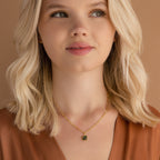 A blonde woman wearing a brown top and the Agate Pendant Necklace, featuring a gold pendant with a small green stone, looks slightly upward.