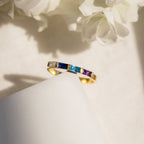 Mothers Baguette Birthstone Ring featuring square blue, purple, and clear gemstones, displayed on a white surface with floral decor.