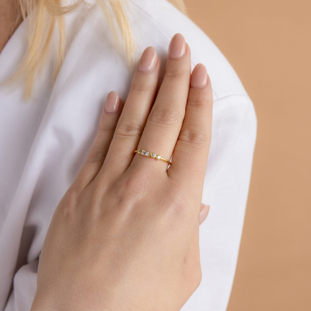 A hand with nude nails wears the Initial Morse Code Ring with small stones, resting on a white sleeve—an elegant, personalized jewelry piece.