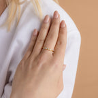 A hand with nude nails wears the Initial Morse Code Ring with small stones, resting on a white sleeve—an elegant, personalized jewelry piece.