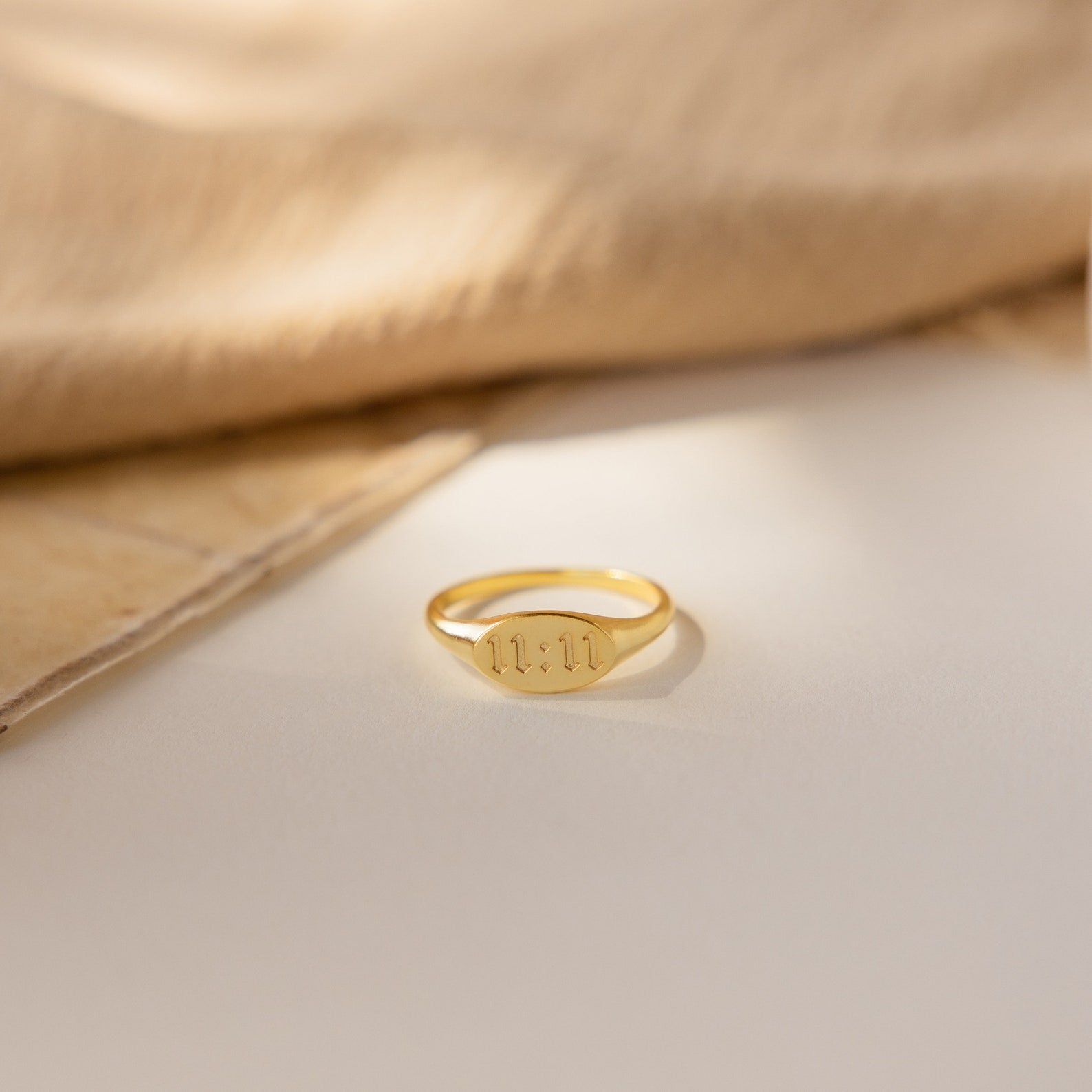 Old English Signet Ring engraved with Roman numerals 11:11, displayed on a light surface with soft fabric in the background—ideal for fans of personalized minimalist jewelry.