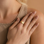 A woman rests her hand on her chest, displaying neutral manicured nails and showcasing the beauty of personalized jewelry with the custom-engraved Carrie Signet Ring featuring numbers.