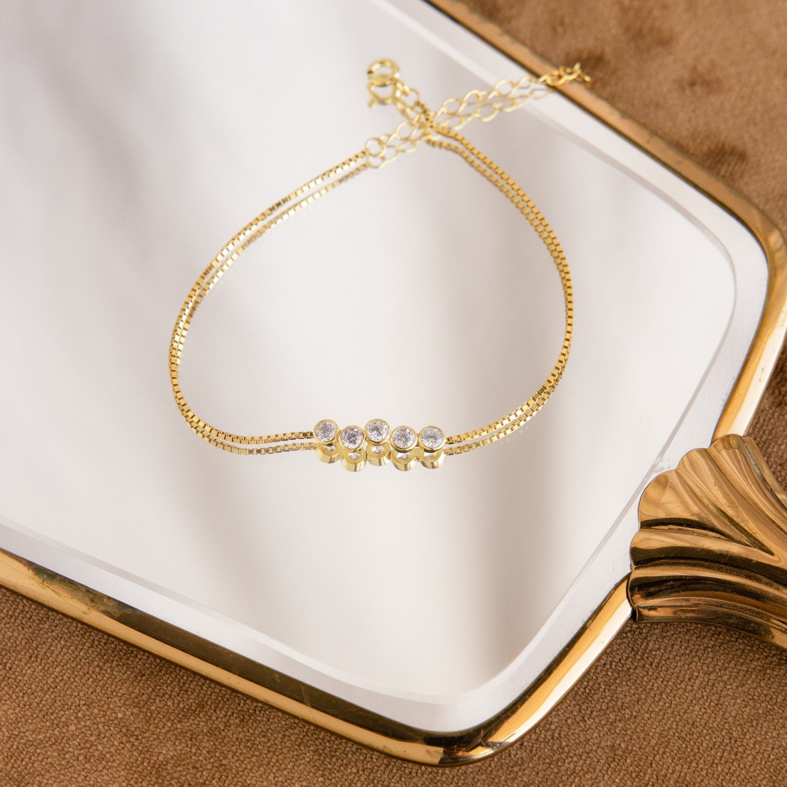 The Cluster Birthstone Bracelet features four round gemstones and is showcased on a white and gold rectangular tray.
