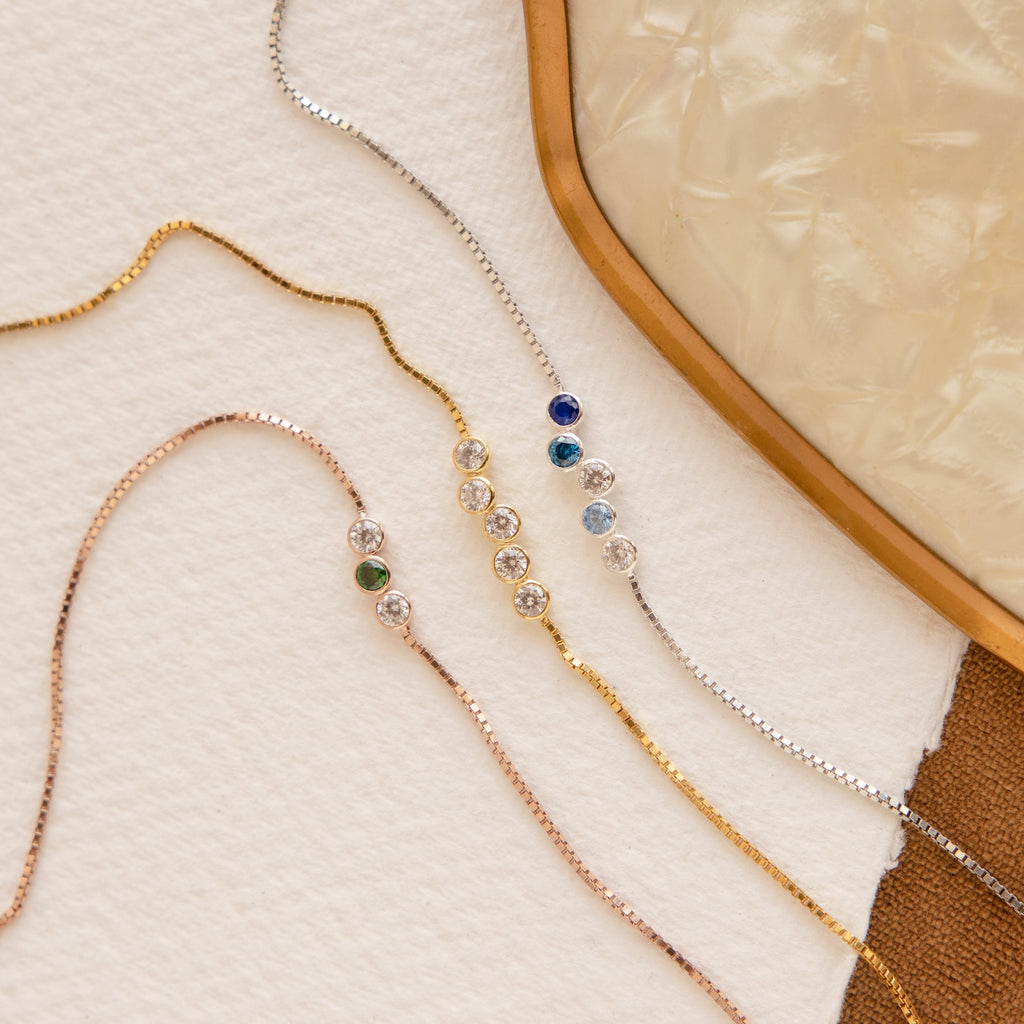 The Cluster Birthstone Bracelet shines in gold, rose gold, and silver on a textured surface.