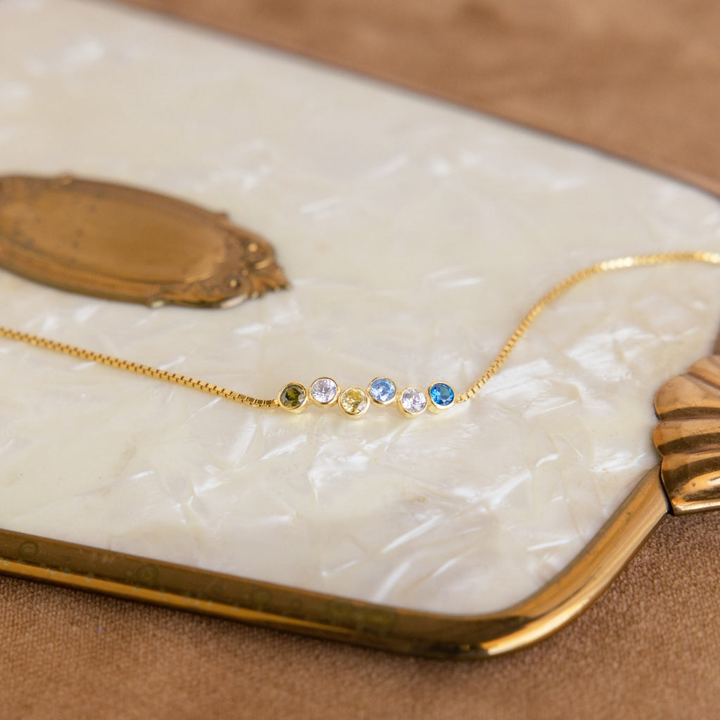 Cluster Birthstone Bracelet featuring five small colorful gemstones, reminiscent of a gold chain necklace, displayed on a vintage mother-of-pearl tray.