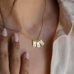 An Old English Mini Tag Necklace with three rectangular gold pendants, each engraved with initials, shown worn on a woman's neck.