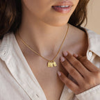 A woman wears the Carrie Mini Tag Necklace with two rectangular pendants, gently touching her collarbone with a manicured hand—a perfect minimalist piece for everyday elegance.