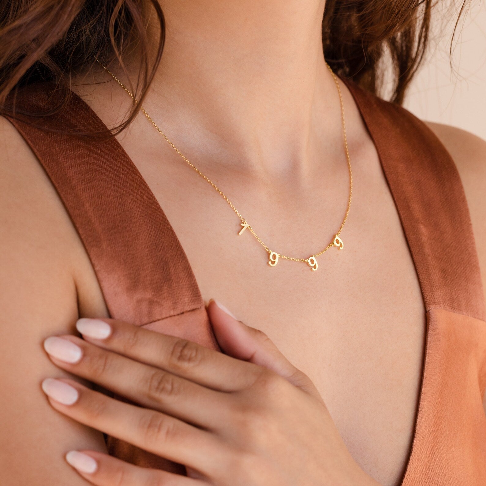 A woman wears the Alice Spaced Number Necklace featuring dangling "1999" numbers, paired with a sleeveless brown top.