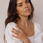 Woman with long, wavy brown hair in a white top showcases the Constellation Ring, posing with her hand near her shoulder.