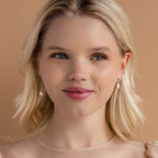 Blonde woman with shoulder-length hair, wearing Asymmetrical Birthstone Drop Earrings and a sheer beige top, smiling slightly.