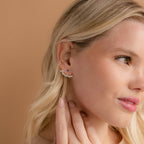 Blonde woman touching her ear, wearing London Name Ear Jackets personalized with "Penelope" against a beige background.