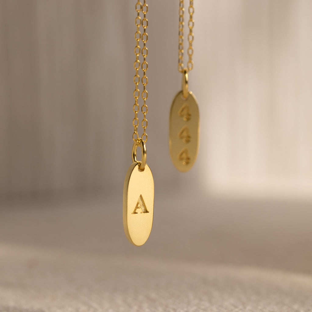 Two Newsletter Oval Tag Necklaces—one engraved with the letter A and the other with 444—create a timeless accessory set.
