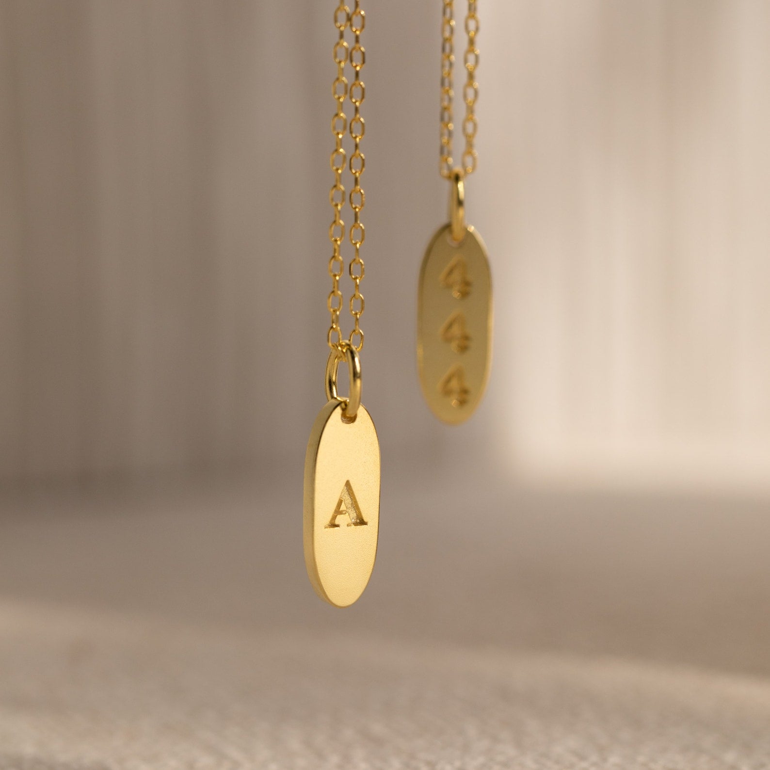 Two Newsletter Oval Tag Necklaces—one engraved with the letter A and the other with 444—create a timeless accessory set.