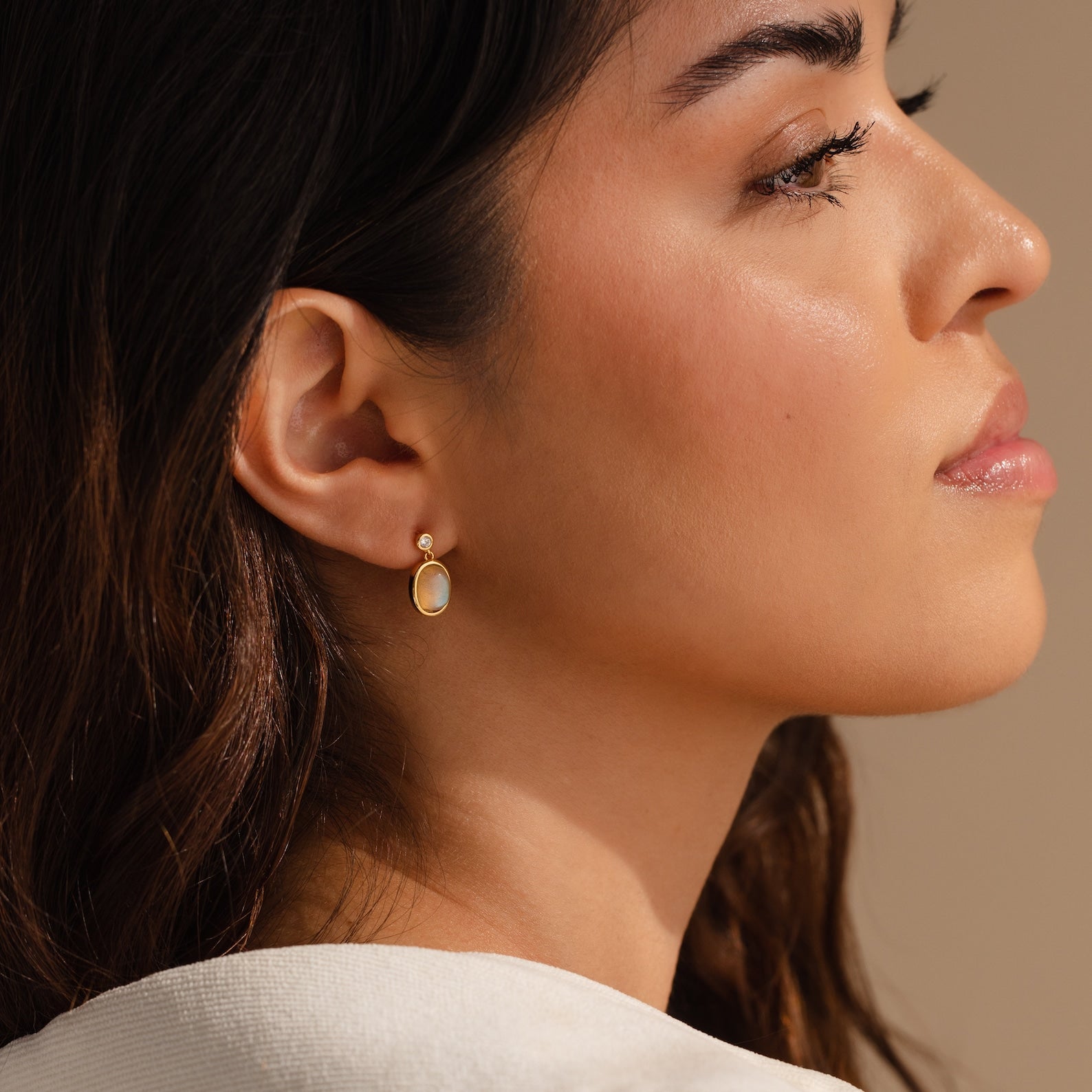 A woman in profile wears Moonstone Drop Earrings, featuring a minimalist gold finish, set against a neutral background.