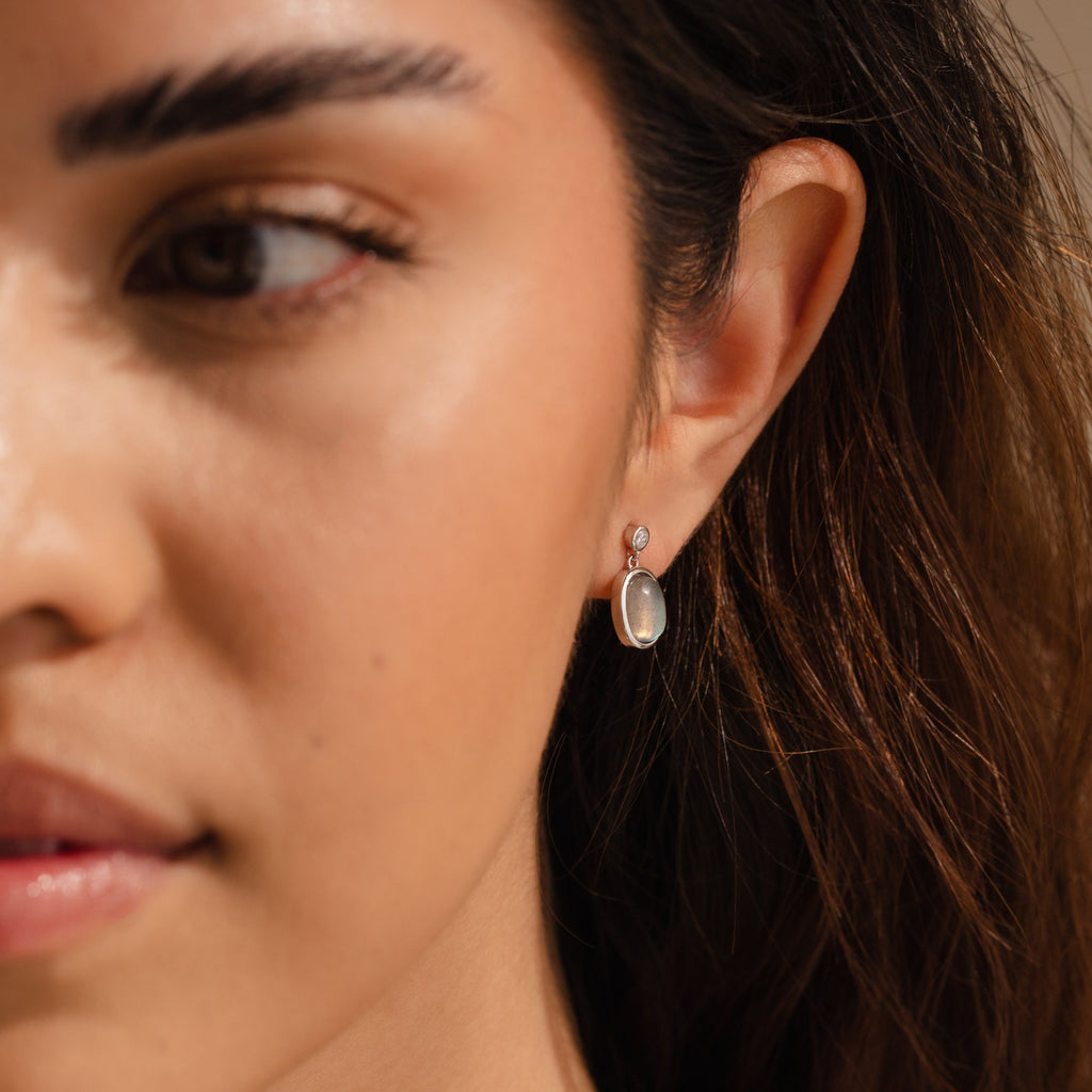 A close-up of a woman wearing Moonstone Drop Earrings, featuring translucent oval stones—an elegant minimalist accessory and a thoughtful graduation gift.