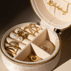 The Round Velvet Jewelry Case is a perfect travel organizer for your favorite pieces, designed to hold gold rings, earrings, a pearl ring, and a gold necklace.
