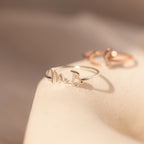 Close-up of the Nella Duo Initial Ring featuring the initials M and B on a soft beige surface—a perfect piece of personalized jewelry.