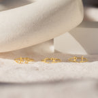 Three Nella Duo Initial Rings with AS, CK, and RL are displayed on a soft beige surface with a white prop—personalized jewelry that's perfect as an anniversary gift.