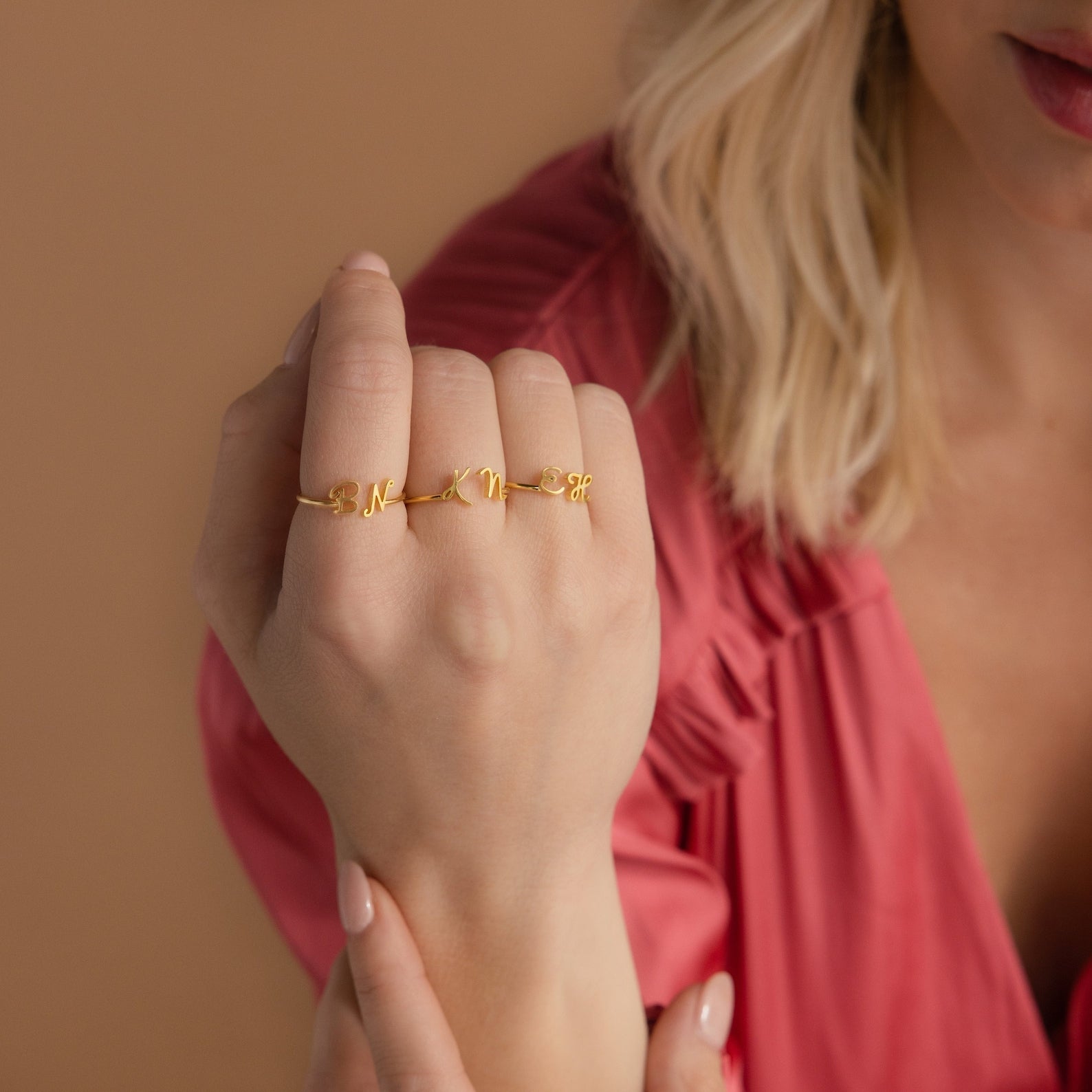 A woman in a pink top displays three gold Dainty Duo Initial Rings with script letters on her fingers, making them a perfect anniversary gift.