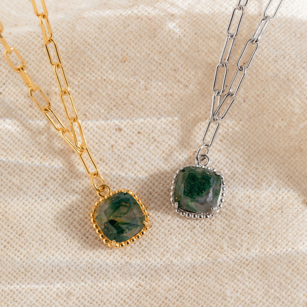 The Agate Pendant Necklace, featuring a handmade green agate gemstone on a gold or silver chain, is displayed against a beige fabric background.