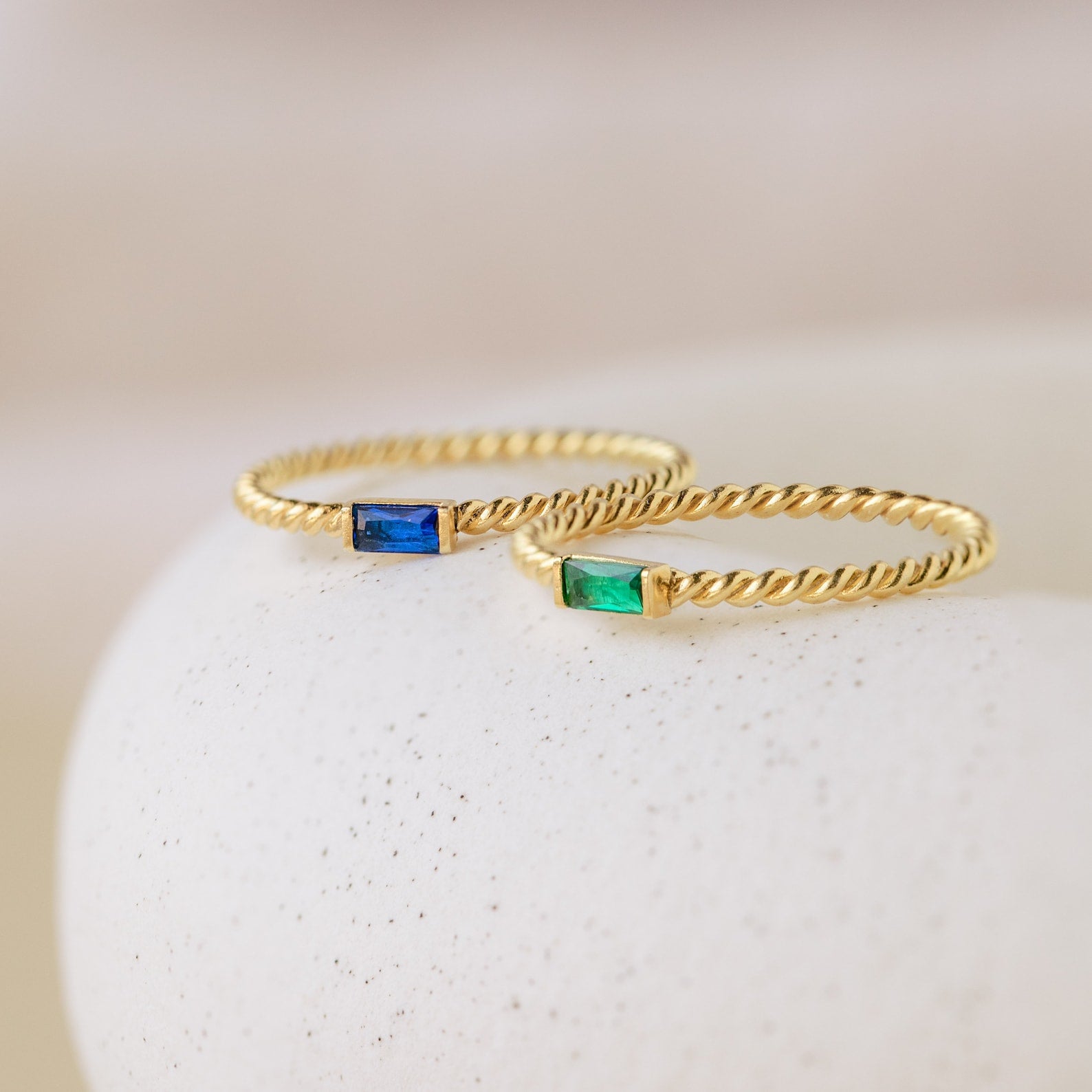 Two Twist Baguette Birthstone Rings—one with a blue rectangular stone and one with a green—add a personalized birthstone accent to your everyday style.