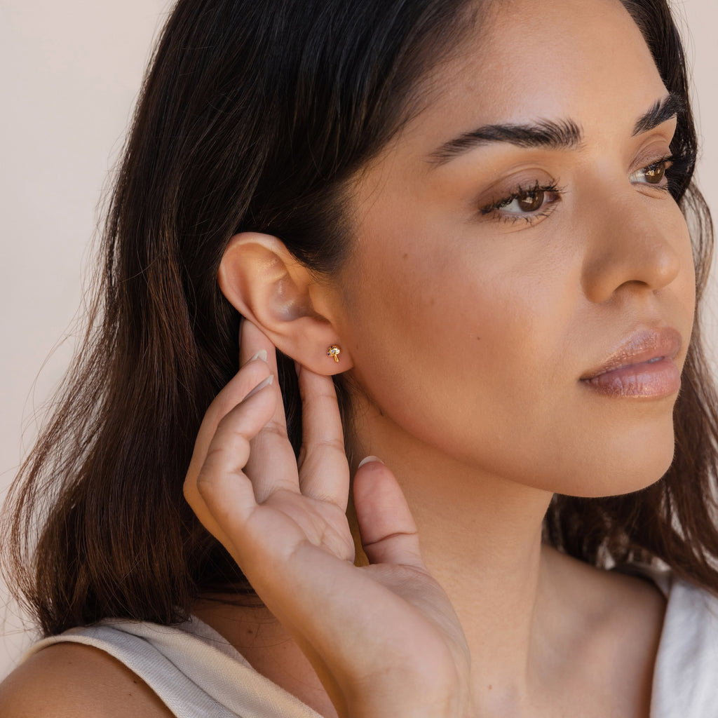 A woman with long brown hair thoughtfully touches her Mushroom Studs, elegant gold earrings inspired by nature.