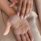 A hand holds two gold Mellow Dainty Initial Necklaces, their delicate pendants visible, as another hand softly touches the palm.