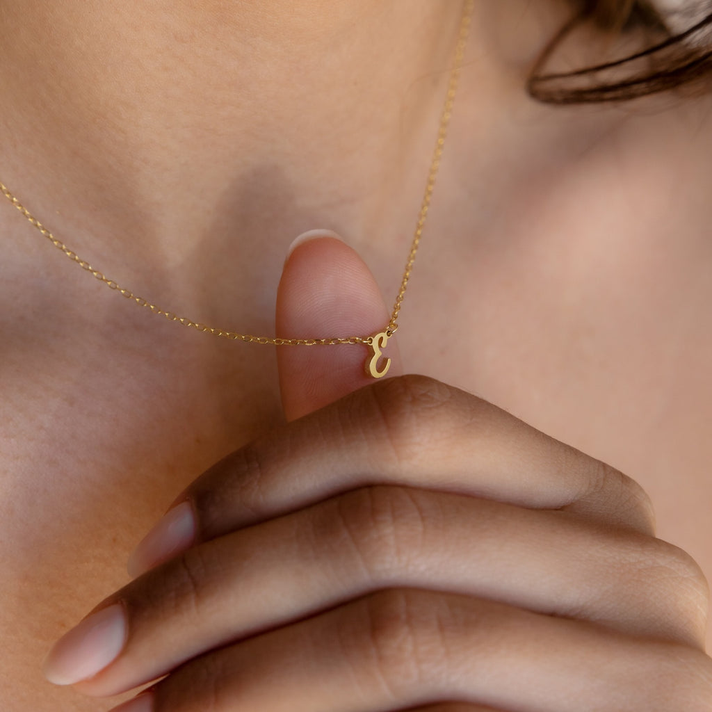 A person holds the Stylish Dainty Initial Necklace, featuring a small gold lowercase "e" pendant, against their chest.