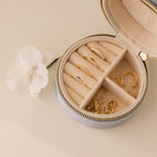 The Round Velvet Jewelry Case is a minimalist organizer, ideal for storing gold rings and earrings at home or while traveling—stylish beside a white flower on any light surface.