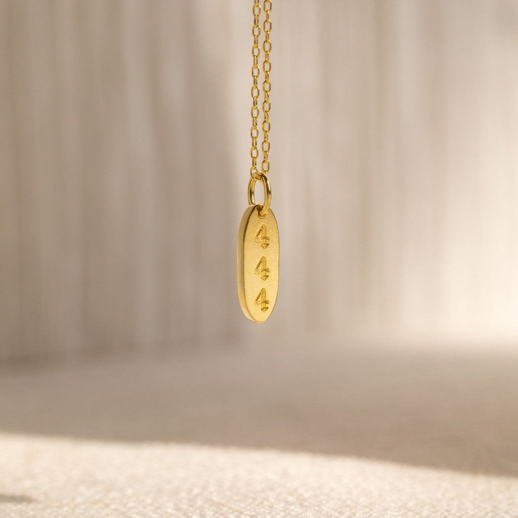 The Old English Oval Tag Necklace features three engraved symbols and can be personalized with initials or a birthstone, displayed against a soft, neutral background.
