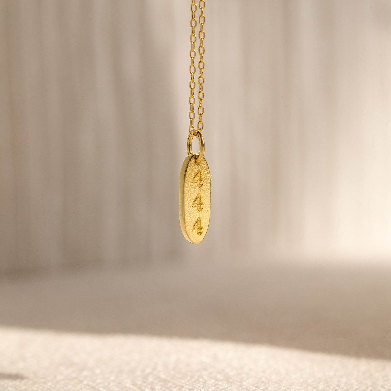The Old English Oval Tag Necklace features three engraved symbols and can be personalized with initials or a birthstone, displayed against a soft, neutral background.