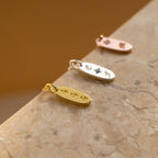 The Old English Oval Tag Necklace features three metal pendants—gold, silver, and rose gold—with engraved initials or symbols, displayed on marble for a personalized touch.