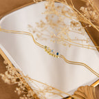 The Cluster Birthstone Bracelet with colorful gemstones is displayed on a mirror, encircled by dried beige flowers.