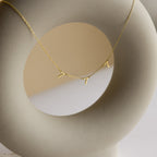 The Alice Spaced Number Necklace, featuring three minimalist charms, is elegantly draped over a smooth, curved beige sculpture.
